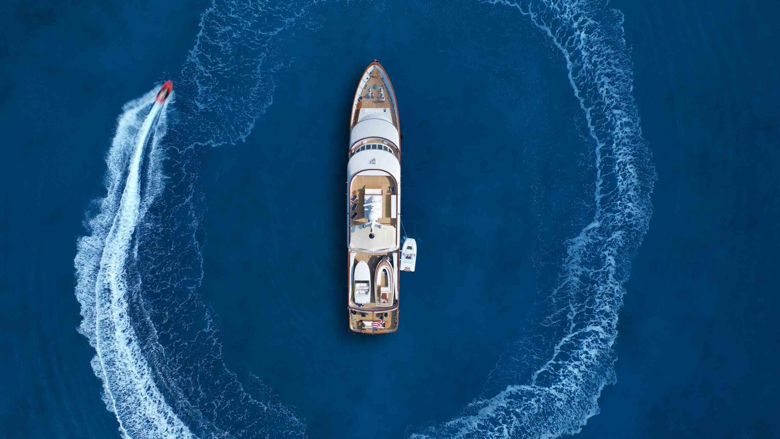 Aerial drone top down photo of stunt man performing extreme stunts and circling with jet ski watercraft over anchored yacht in deep blue ocean sea